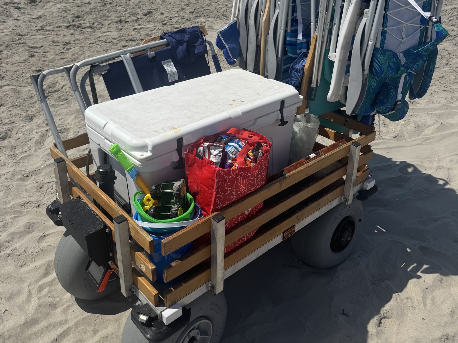 Looking into the loaded bed: cooler, snack bag, and kids' beach toys stacked between the wooden rails